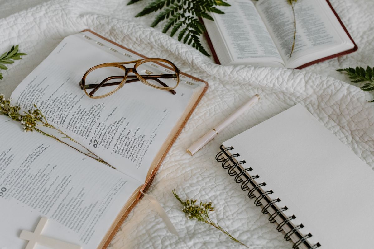 An open Bible with reading glasses, a notebook, and pen
